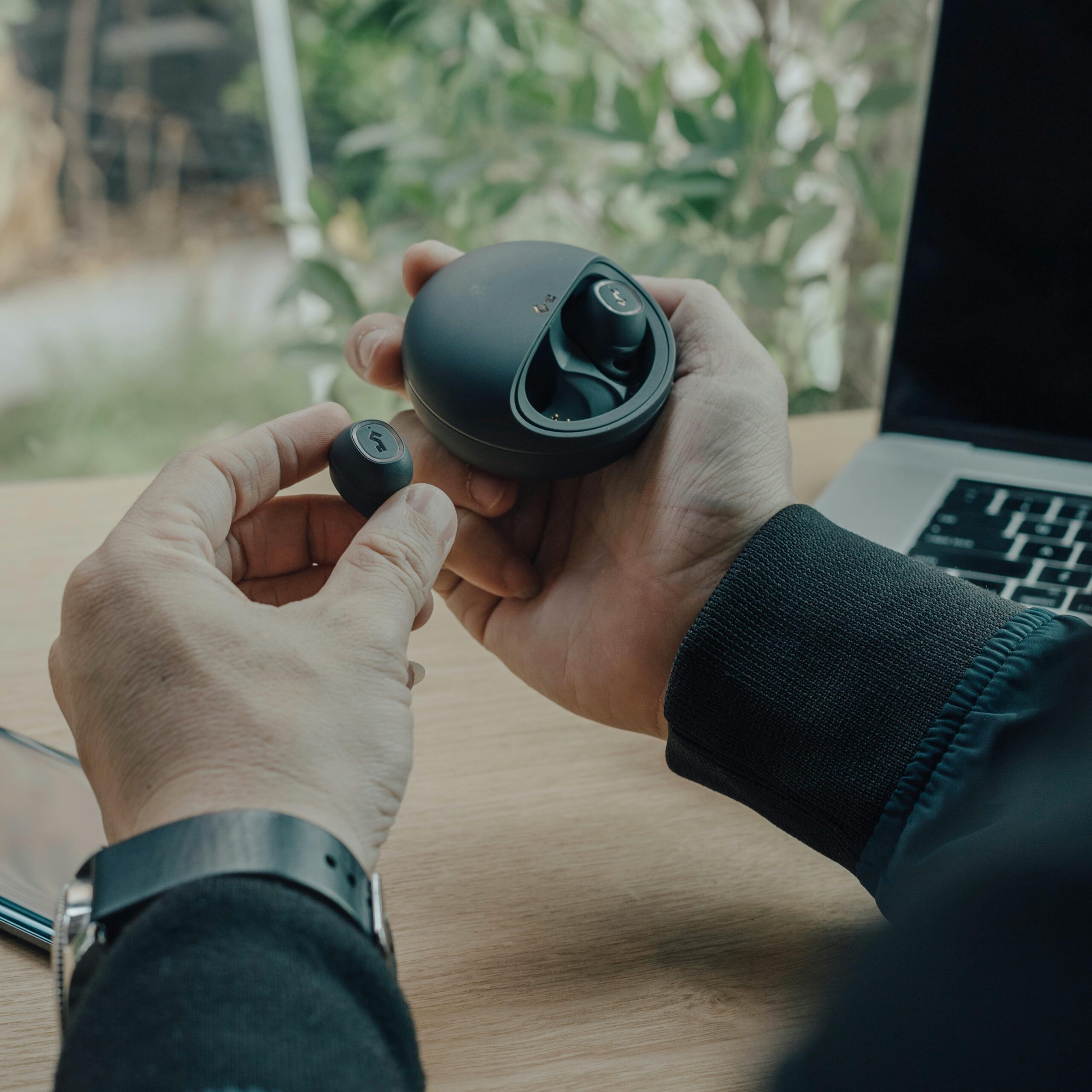 our-services-01 Unrecognizable male sitting at wooden table with laptop and holding true wireless earphones placed in charging case